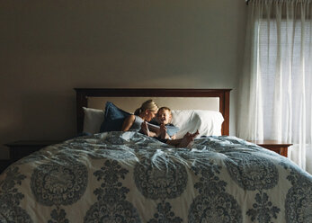 Happy mother and son reading book while relaxing on bed - CAVF14520