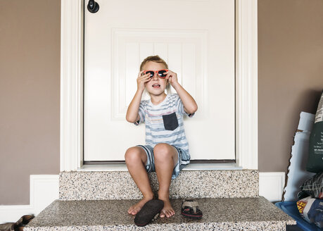 Boy wearing sunglasses while sitting on doorway - CAVF14532