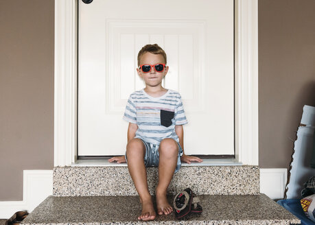 Full length of boy wearing sunglasses sitting on doorway - CAVF14533