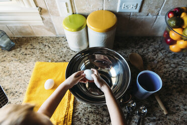 High angle view of boy breaking eggs in bowl at kitchen counter - CAVF14539