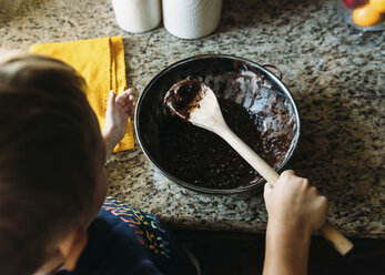 Hochformatige Ansicht eines Jungen, der in der Küche Schokoladensauce herstellt - CAVF14540