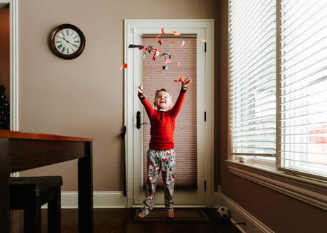 Fröhlicher Junge, der Konfetti wirft, während er auf der Fußmatte neben der Tür zu Hause steht - CAVF14559
