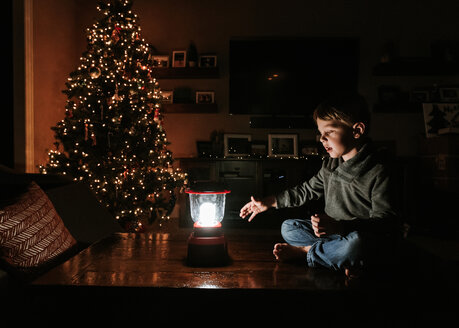 Boy with lantern sitting on table by Christmas tree at home - CAVF14560