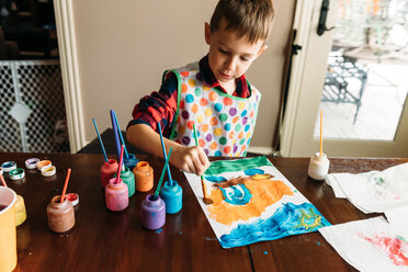 Junge malt Bild auf Papier am Tisch im Haus - CAVF14561