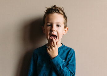 Portrait of boy touching teeth while standing against wall at home - CAVF14569