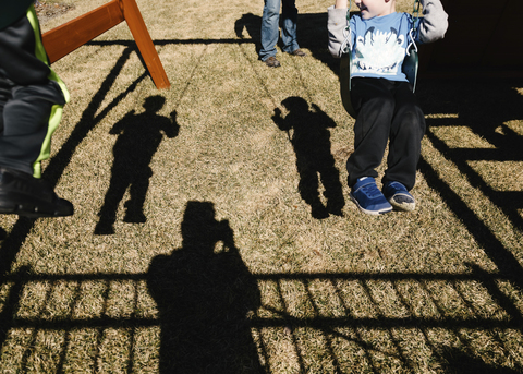 Schatten von schwingenden Söhnen, während der Vater auf dem Spielplatz steht, lizenzfreies Stockfoto