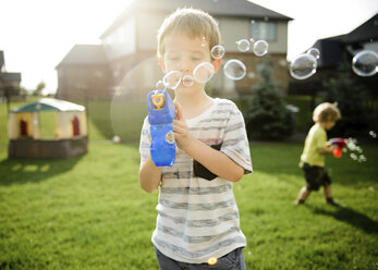 Brothers playing with bubble toy guns while standing in yard - CAVF14592