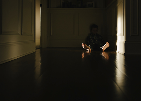 Junge sitzt auf dem Boden in der Dunkelkammer zu Hause, lizenzfreies Stockfoto