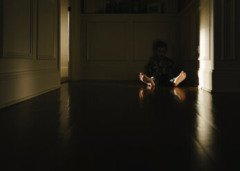 Boy sitting on floor in darkroom at home - CAVF14597