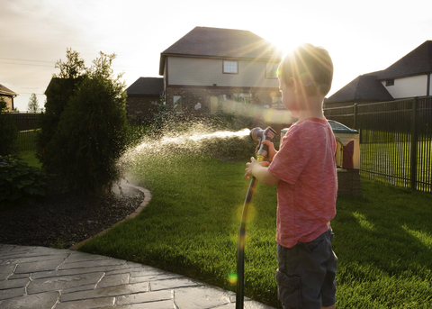 Boy watering plants while standing in yard stock photo