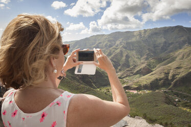 Rückansicht einer Frau, die mit ihrem Smartphone vor einem Berg fotografiert - CAVF14637