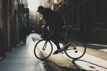 Seitenansicht eines Mannes, der bei Sonnenuntergang auf dem Fußweg Fahrrad fährt - CAVF14683