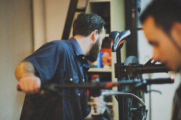 Mechanic repairing bicycle while customer standing at workshop - CAVF14691