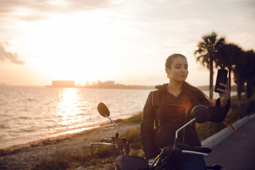 Schöne Frau klickend selfie beim Sitzen auf Motorrad während Sonnenuntergang - CAVF14720