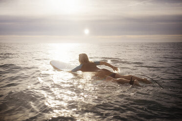 Rückansicht einer Surferin, die bei Sonnenuntergang auf einem Surfbrett im Meer liegt - CAVF14738