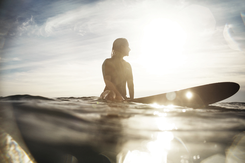 Oberflächenniveau einer Frau, die im Sommer auf einem Surfbrett im Meer sitzt, lizenzfreies Stockfoto