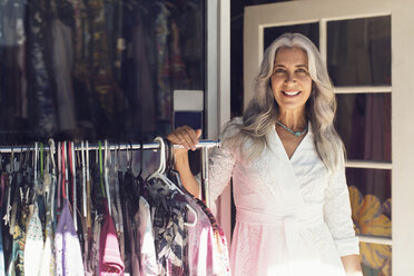 Porträt einer lächelnden reifen Frau, die an einem Kleiderständer vor einem Geschäft steht - CAVF14761