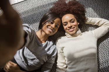 Overhead portrait of happy female friends lying on rug at home - CAVF14771