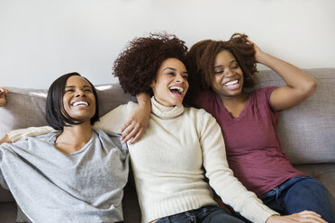 Cheerful female friends sitting on sofa at home - CAVF14774