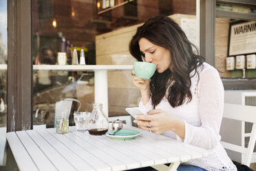 Frau trinkt Kaffee und benutzt ihr Smartphone in einem Straßencafé - CAVF14803