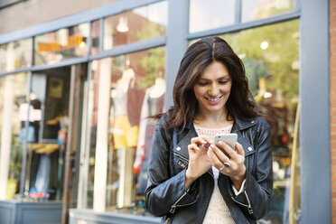 Happy woman using smart phone outside shop - CAVF14821