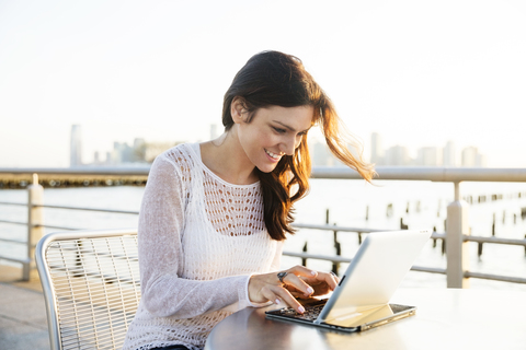 Glückliche Frau mit Tablet-Computer in einem Café an der Promenade bei Sonnenuntergang, lizenzfreies Stockfoto