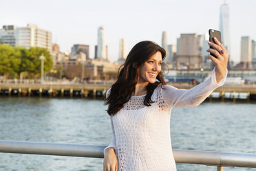 Happy woman taking selfie while standing on promenade with One World Trade Center in background - CAVF14838