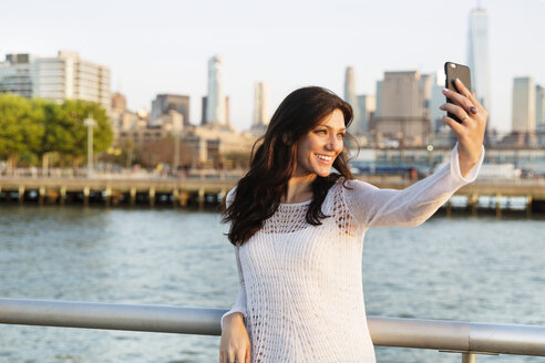 Glückliche Frau, die ein Selfie macht, während sie auf der Promenade mit dem One World Trade Center im Hintergrund steht - CAVF14838