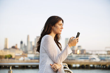 Seitenansicht einer Frau, die ihr Smartphone in der Hand hält, während sie an einem Beobachtungspunkt bei Sonnenuntergang steht - CAVF14839