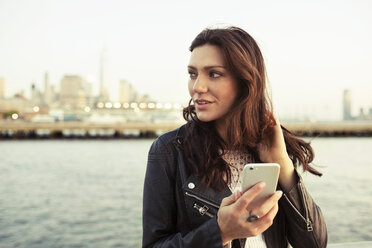 Thoughtful woman holding smart phone with One World Trade Center in background - CAVF14841