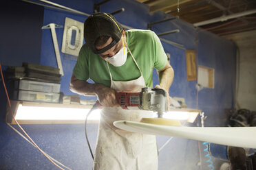 Worker using sander while making surfboard in workshop - CAVF14843