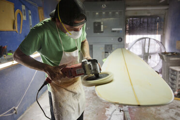 Male worker using sander on surfboard in workshop - CAVF14844