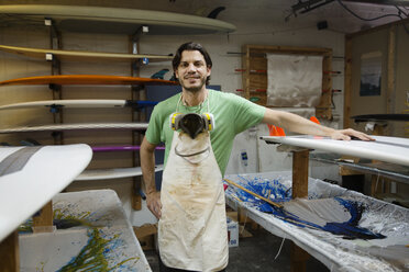 Porträt eines lächelnden Mannes, der neben Surfbrettern in einer Werkstatt steht - CAVF14852