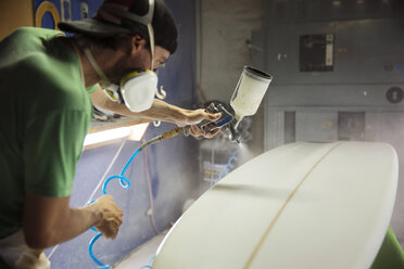 Concentrated worker spraying white paint on surfboard - CAVF14859