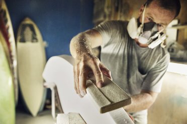 Mid adult man shaping edge of surfboard at workshop - CAVF14867