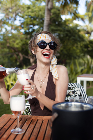 Cheerful woman pouring champagne in glass at table stock photo