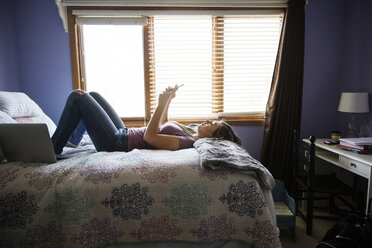 Girl lying on bed and using phone at home - CAVF14954