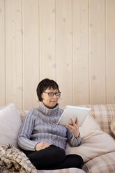Ältere Frau benutzt einen Tablet-Computer, während sie zu Hause auf dem Sofa sitzt - CAVF14965