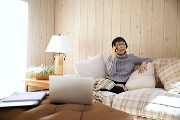 Ältere Frau benutzt ein Smartphone, während sie zu Hause auf dem Sofa sitzt - CAVF14972