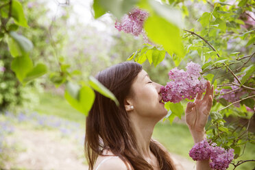 Seitenansicht einer schönen Frau, die im Park an Blumen riecht - CAVF15025