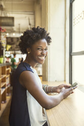 Porträt einer glücklichen Frau mit einem Smartphone in einem Geschäft - CAVF15032