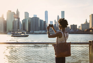 Rear view of woman photographing city skyline during sunset - CAVF15044