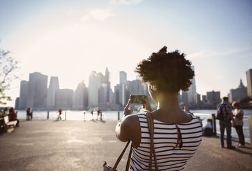 Rear view of woman photographing city skyline from observation point during sunset - CAVF15045