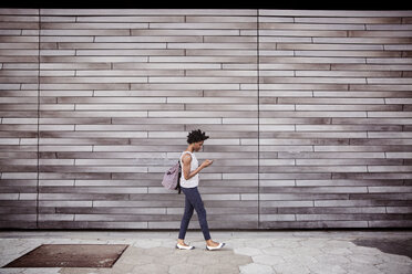 Seitenansicht einer Frau, die ein Smartphone benutzt, während sie gegen eine Wand läuft - CAVF15049