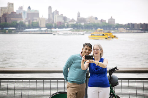 Glückliches reifes Paar, das ein Selfie macht, während es auf der Promenade am Fluss in der Stadt steht - CAVF15060