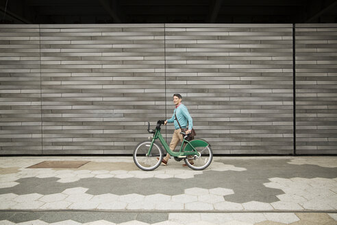Seitenansicht eines reifen Mannes, der mit seinem Fahrrad auf einem Fußweg an einer Mauer spazieren geht - CAVF15063