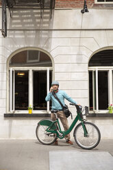 Älterer Mann, der ein Smartphone benutzt, während er mit dem Fahrrad vor einem Gebäude steht - CAVF15066