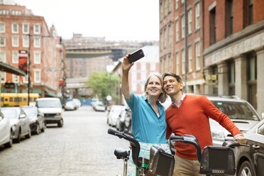 Mature couple taking selfie while standing with bicycles on city street - CAVF15077