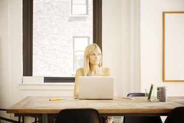Thoughtful businesswoman sitting with laptop at desk in creative office - CAVF15083