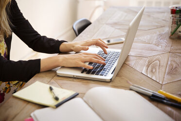 Cropped image of businesswoman using laptop at desk in office - CAVF15085